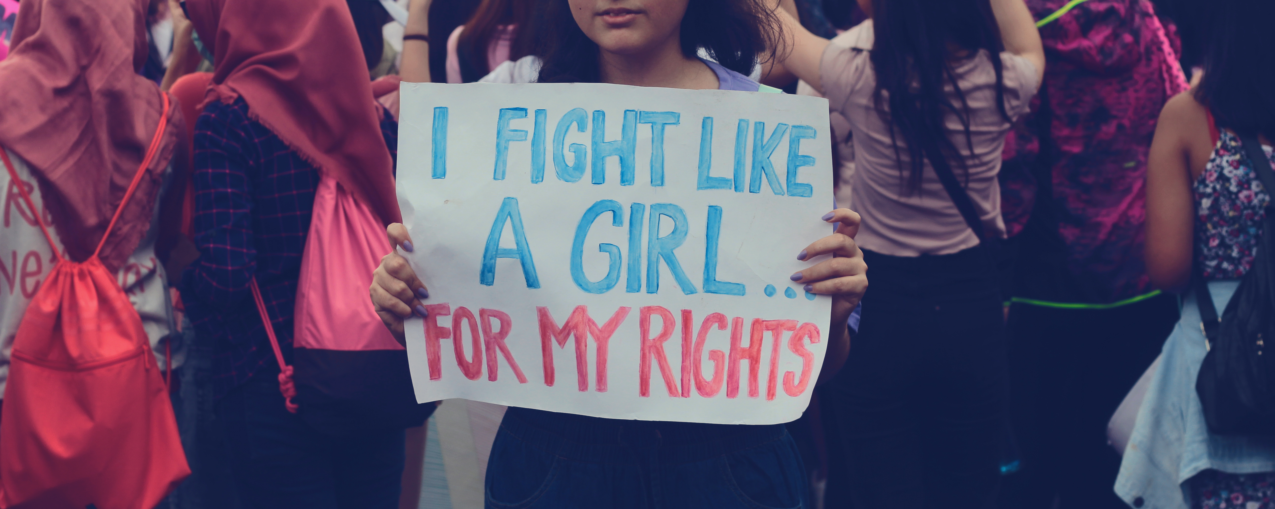 Young woman holds sign at protest which reads: I fight like a girl for my rights