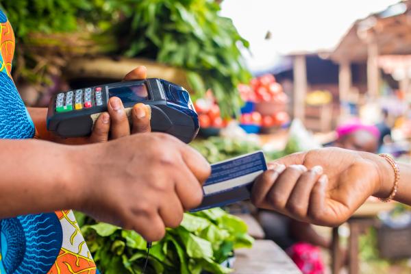 African woman uses card machine to process payment at her market stall