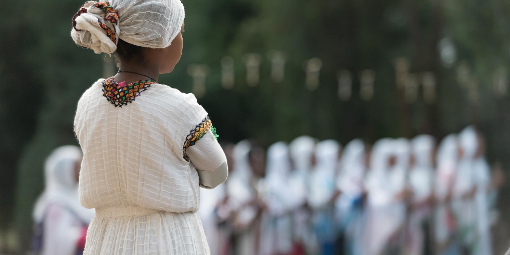 Young Ethiopian woman wearing traditional dress watches crowd from a distance