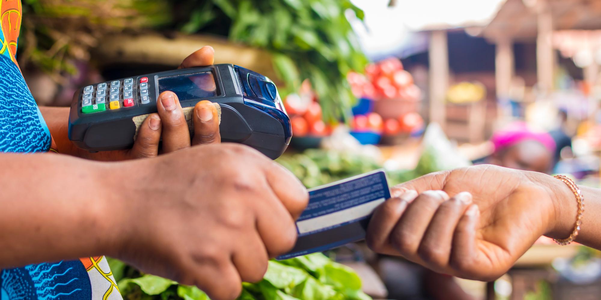 African woman uses card machine to process payment at her market stall