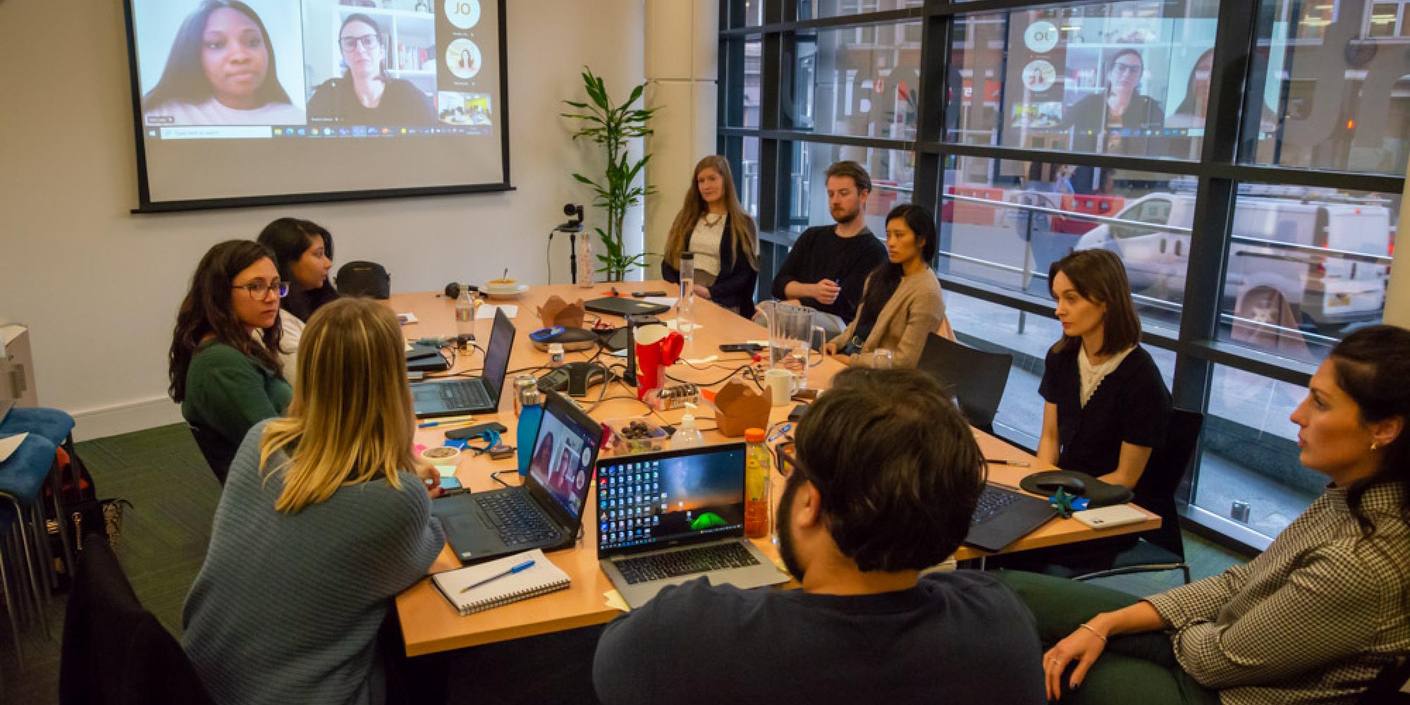 Photo of team working collaboratively in office space, other colleagues joining remotely