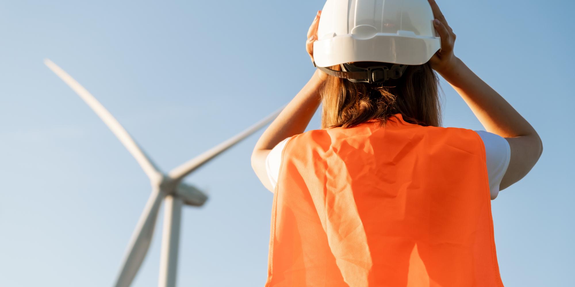 Photo of woman staring at windmill, wearing high visibility jacket and hard hat