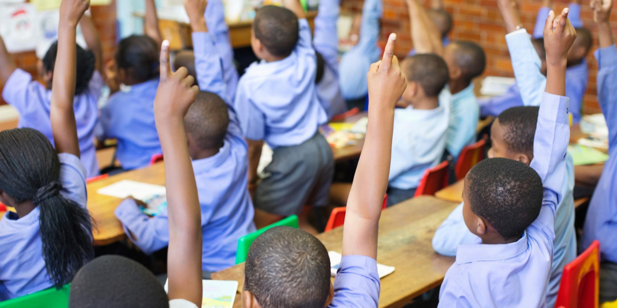 image of children in a classroom raising hands